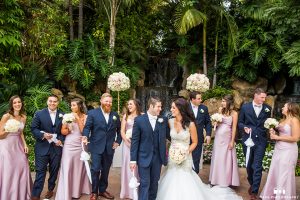 San diego outdoor wedding at the grand tradition bride mermaid style gown with illusion back and straps with plunging neckline and groom navy suit with matching vest and white dress shirt with white bow tie and white floral boutonniere with bridesmaids long pink dresses with groomsmen navy suits with long ties