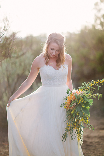 Anza valley rustic outdoor wedding at the alpaca farm bride strapless chiffon gown with a sweetheart neckline holding green and yellow floral bridal bouquet while holding up side of dress wedding photo idea for bride