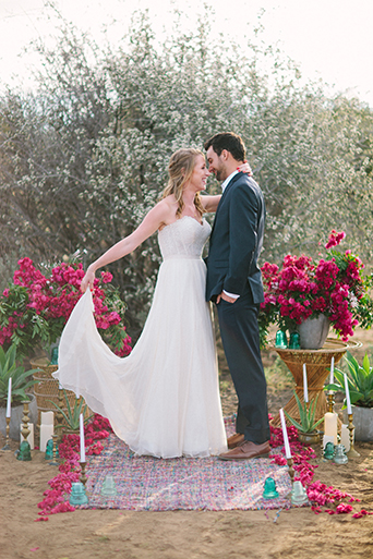 Anza valley rustic outdoor wedding at the alpaca farm bride strapless chiffon gown with a sweetheart necklace holding green and yellow floral bridal bouquet with groom navy blue suit with white dress shirt and no tie standing by pink floral arch for ceremony