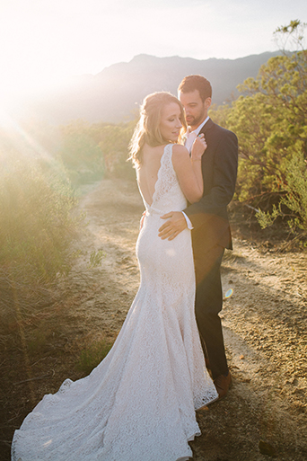 Anza valley rustic outdoor wedding at the alpaca farm bride chiffon gown with lace straps and open back design with wedding ring and groom navy blue suit with white dress shirt and no tie wedding photo idea hugging at sunset