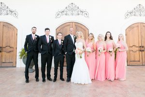 Temecula outdoor wedding at villa de amore vineyard bride strapless mermaid style gown with crystal belt and medium veil with groom black tuxedo with white dress shirt and white bow tie with matching vest and white floral boutonniere with bridesmaids long pink dresses and groomsmen black tuxedo with pink ties