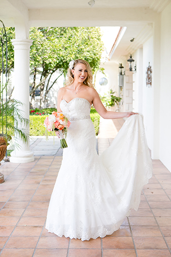 Temecula outdoor wedding at villa de amore vineyard bride strapless mermaid style gown with crystal belt and medium veil holding bottom of dress with white and pink floral bridal bouquet