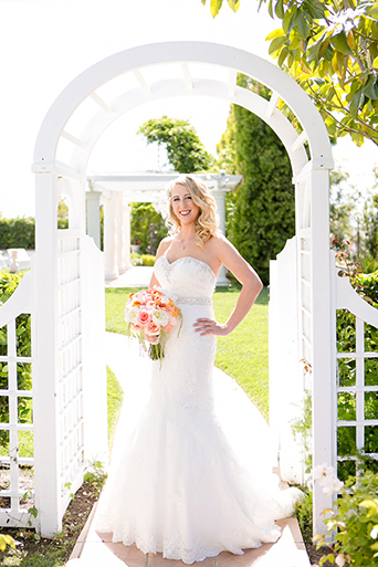 Temecula outdoor wedding at villa de amore vineyard bride strapless mermaid style gown with crystal belt and medium veil holding bottom of dress with white and pink floral bridal bouquet