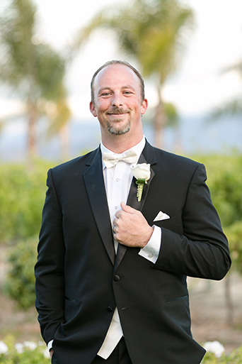 Temecula outdoor wedding at villa de amore vineyard groom black tuxedo with white dress shirt and white bow tie with matching vest and white floral boutonniere
