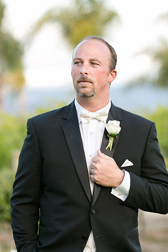 Temecula outdoor wedding at villa de amore vineyard groom black tuxedo with white dress shirt and white bow tie with matching vest and white floral boutonniere
