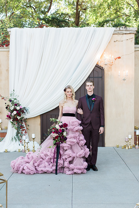 Los angeles valentine theme wedding shoot at the gardens at los robles bride pink ballgown dress with ruffled skirt and dark pink and white floral bridal bouquet with groom burgundy tuxedo with black dress shirt and black bow tie with red floral boutonniere