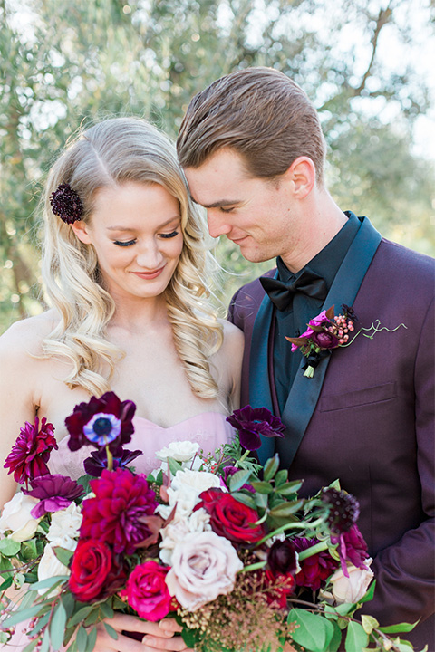 Los angeles valentine theme wedding shoot at the gardens at los robles bride pink ballgown dress with ruffled skirt and dark pink and white floral bridal bouquet with groom burgundy tuxedo with black dress shirt and black bow tie with red floral boutonniere smiling close up