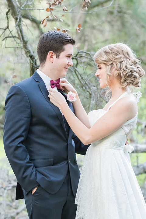 Valentine styled wedding shoot bride chiffon gown with halter straps and sweetheart neckline with groom navy blue suit with notch lapel with matching vest and white dress shirt with red bow tie and white floral boutonniere hugging