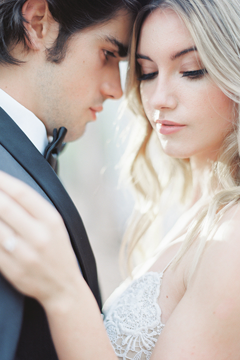 Into the woods outdoor romantic wedding shoot bride chiffon gown with thin spahetti straps and strap design on back with lace detail and sweetheart neckline with groom charcoal grey tuxedo coat with black lapels and black pants with white dress shirt and black bow tie hugging