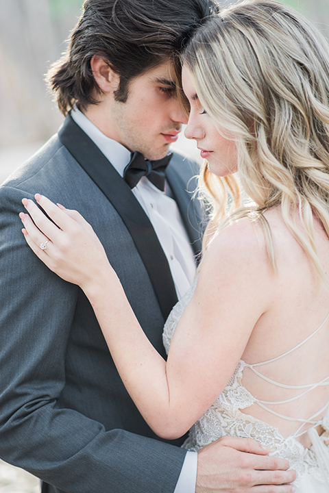 Into the woods outdoor romantic wedding shoot bride chiffon gown with thin spahetti straps and strap design on back with lace detail and sweetheart neckline with groom charcoal grey tuxedo coat with black lapels and black pants with white dress shirt and black bow tie hugging