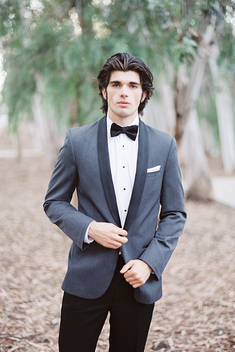 Into the woods outdoor romantic wedding shoot groom charcoal grey tuxedo with black lapels and black pants with white dress shirt and black bow tie with white pocket square holding jacket