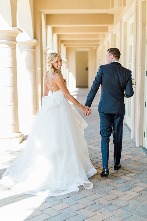 Laguna beach wedding bride ball gown with thin spaghetti straps and a sweetheart neckline with groom navy blue tuxedo with black shawl lapel and white dress shirt with black bow tie and white floral boutonniere holding hands after first