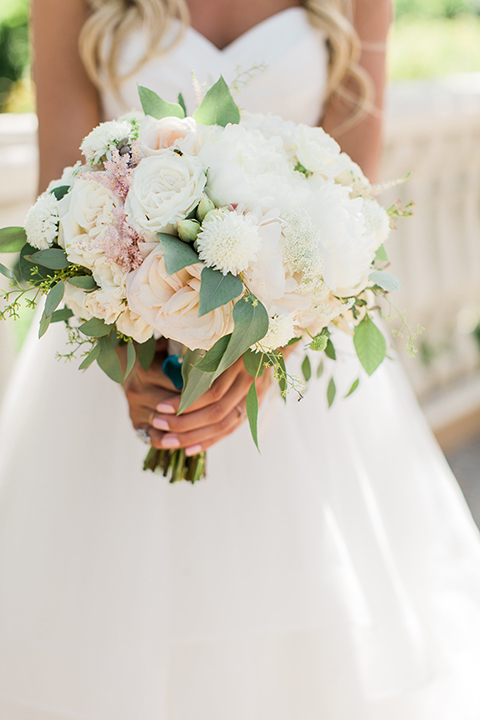 Laguna beach wedding bride ball gown with thin spaghetti straps and a sweetheart neckline holding white and green floral bridal bouquet