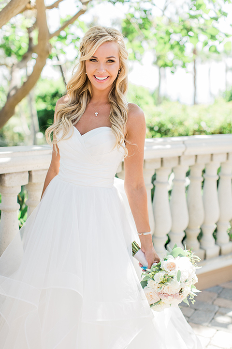 Laguna beach wedding bride ball gown with thin spaghetti straps and a sweetheart neckline holding white and green floral bridal bouquet