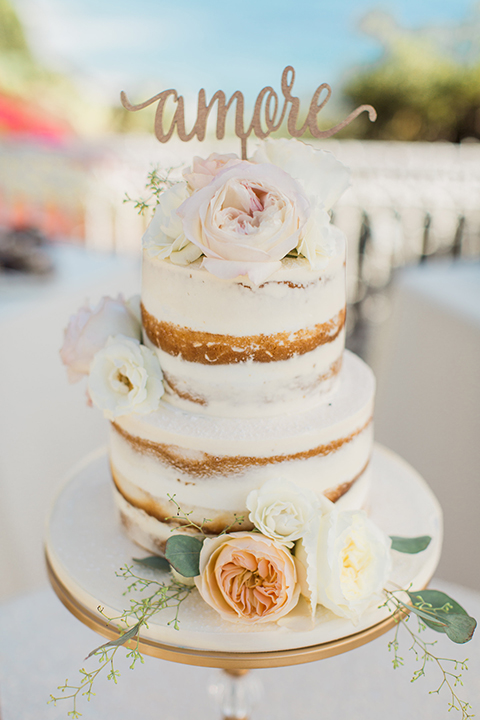 Laguna beach wedding two tier white wedding cake with light pink and white flower decor on top and on side with gold calligraphy cake topper on white tray wedding photo idea for cake