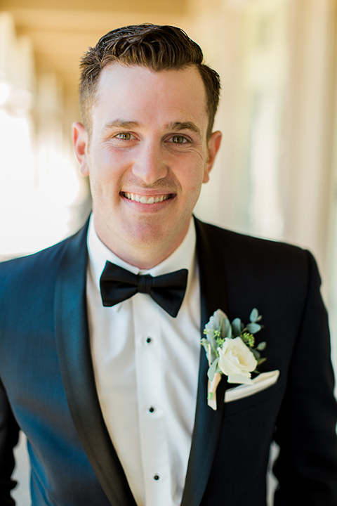 Laguna beach wedding groom navy blue tuxedo with a black shawl lapel and white dress shirt with black bow tie and white pocket square with white floral boutonniere