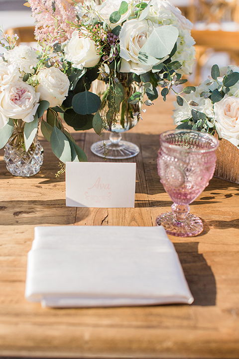 Laguna beach wedding table set up light brown wood table with light pink glasses and white and pink flower centerpiece decor with geometric shaped decor and white place settings with light brown chairs