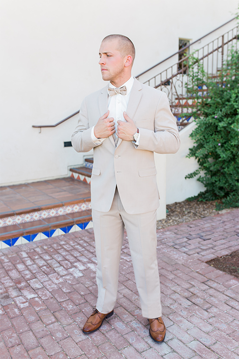 Temecula outdoor wedding at ponte winery groom tan suit with matching vest and white dress shirt with matching tan bow tie holding jacket