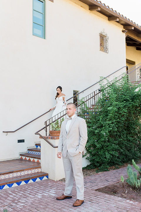 Temecula outdoor wedding at ponte winery bride form fitting lace gown with long sleeves and illusion open back design with sweetheart neckline and groom tan suit with matching vest and white dress shirt with matching tan bow tie and white floral boutonniere bride walking down the stairs for first look