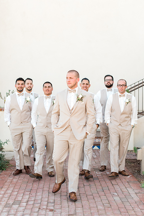Temecula outdoor wedding at ponte winery groom tan suit with matching vest and white dress shirt with matching tan bow tie with white floral boutonniere with groomsmen tan suits with matching tan vests and tan bow ties walking