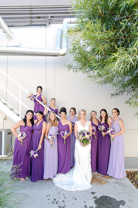 Temecula outdoor wedding at callaway winery bride form fitting lace gown with thick straps and open back design with plunging neckline with white and purple floral bridal bouquet with bridesmaids long purple dresses with white and purple floral bridal bouquet