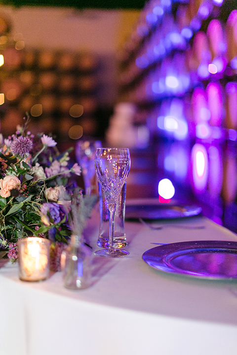Temecula outdoor wedding at callaway winery table set up with white table linen and purple napkin linen decor with dark chairs and white and purple flower centerpiece decor with silver place settings with heart decor and candles
