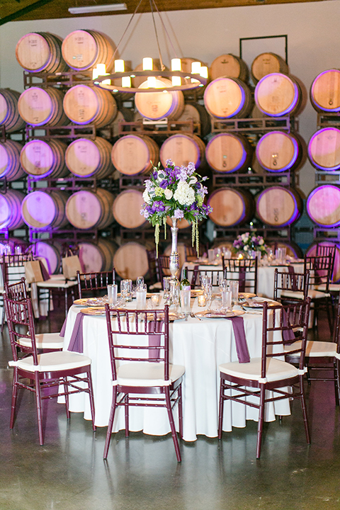 Temecula outdoor wedding at callaway winery table set up with white table linen and purple napkin linen decor with dark chairs and white and purple flower centerpiece decor with silver place settings with heart decor and candles