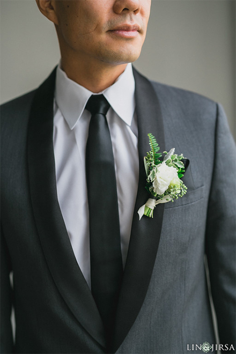 Downtown los angeles wedding groom charcoal grey tuxedo with black shawl lapel and black pants with white dress shirt with long black skinny tie and white floral boutonniere close up