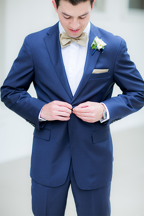 San diego wedding at the crossings carlsbad groom cobalt blue suit with white dress shirt and gold bow tie with matching pocket square and white floral boutonniere buttoning jacket