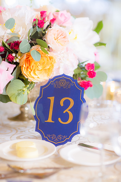 San diego wedding at the crossings carlsbad table set up with white table linen and gold chairs with white and pink flower centerpiece decor with white place settings and candle decor with blue and gold table numbers