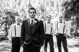 San diego wedding at green gables estate groom black shawl lapel tuxedo with matching vest and white dress shirt with long black skinny tie and white floral boutonniere with groomsmen bow ties and suspenders black and white photo