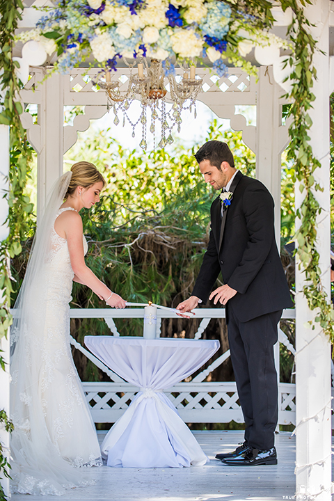 San diego wedding at green gables estate bride form fitting lace gown with a long train and high illusion neckline with long veil and groom black shawl lapel tuxedo with matching vest and white dress shirt with long black skinny tie and white floral boutonniere ceremony