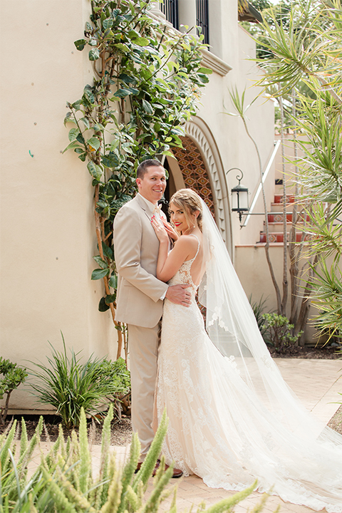 Los angeles wedding at los verdes golf club bride form fitting gown with lace detail and low back design with thin straps and long veil with groom tan notch lapel suit with matching vest and white dress shirt with matching tan bow tie and white pocket square with white and red floral boutonniere