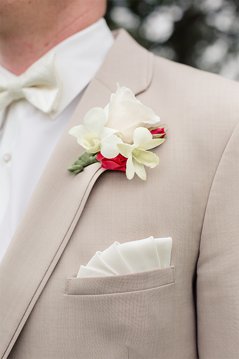 Los angeles wedding at los verdes golf club groom tan notch lapel suit with matching vest and white dress shirt with matching tan bow tie and white pocket square with white and red floral boutonniere close up