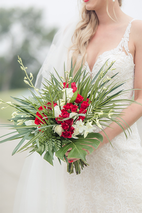 Los angeles wedding at los verdes golf club bride form fitting gown with lace detail and low back design with thin straps and long veil holding red and white floral bridal bouquet close up