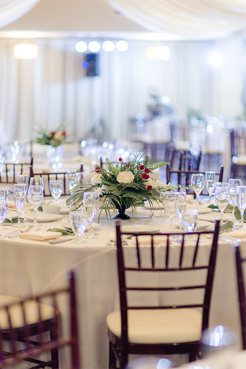 Los verdes golf club wedding table set up white table linens with dark chairs and white and green and red flower centerpiece decor with wine glasses and table numbers