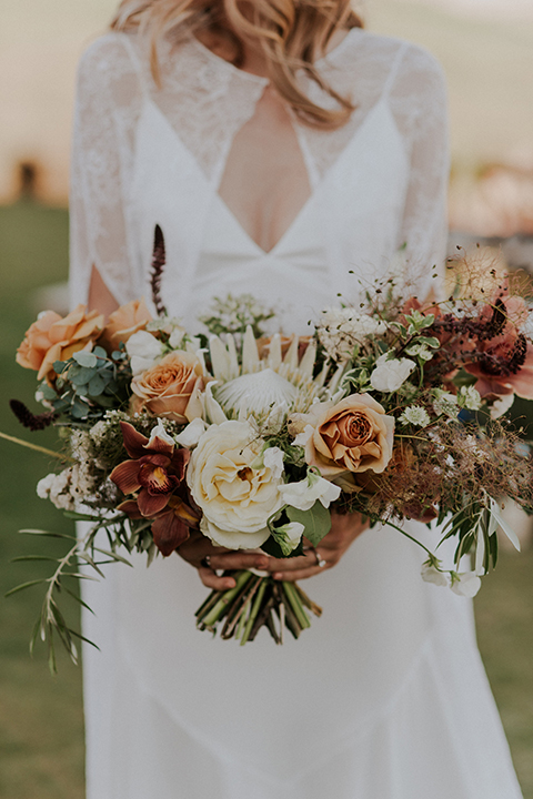 San diego outdoor wedding shoot at the san diego zoo and safari park bride white chiffon gown with lace sleeves and thin straps with plunging neckline holding white and orange floral bridal bouquet close up