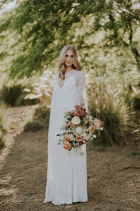 San diego outdoor wedding shoot at the san diego zoo and safari park bride white chiffon gown with lace sleeves and thin straps with plunging neckline holding white and orange floral bridal bouquet
