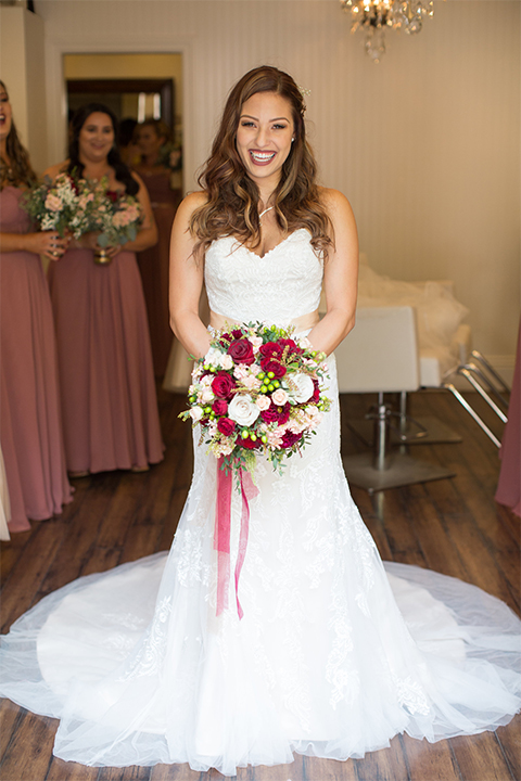 Temecula outdoor rustic wedding at lake oak meadows bride form fitting strapless gown with sweetheart neckline and lace detail with long veil with necklace holding white and red floral bridal bouquet with red ribbon decor