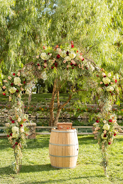 Temecula outdoor rustic wedding at the lake oak meadows ceremony decor wine barrel with wood tree stump and black and white chalkboard design on the grass wedding photo idea for ceremony decor with floral arch with white and red flowers and greenery
