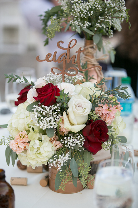 Temecula outdoor rustic wedding at the lake oak meadows table set up with white table linen and white and red flower decor with greenery florals and white initial letters with white place settings and gold table numbers