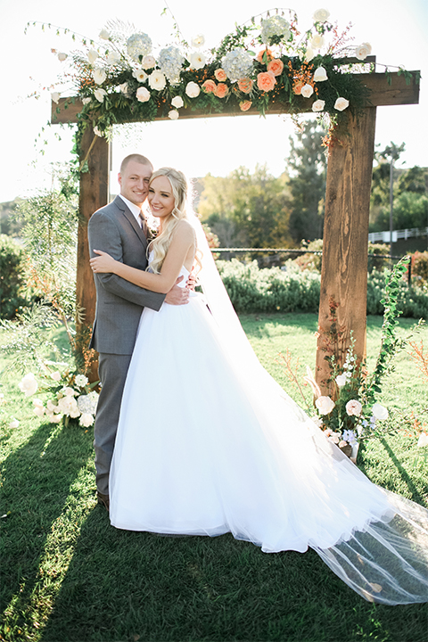 Southern california wedding at riverview free church bride strapless ball gown with a sweetheart neckline and tulle skirt with a long veil and braided hairstyle with groom grey notch lapel suit with matching vest and white dress shirt with long grey tie and light blue and green floral boutonniere hugging