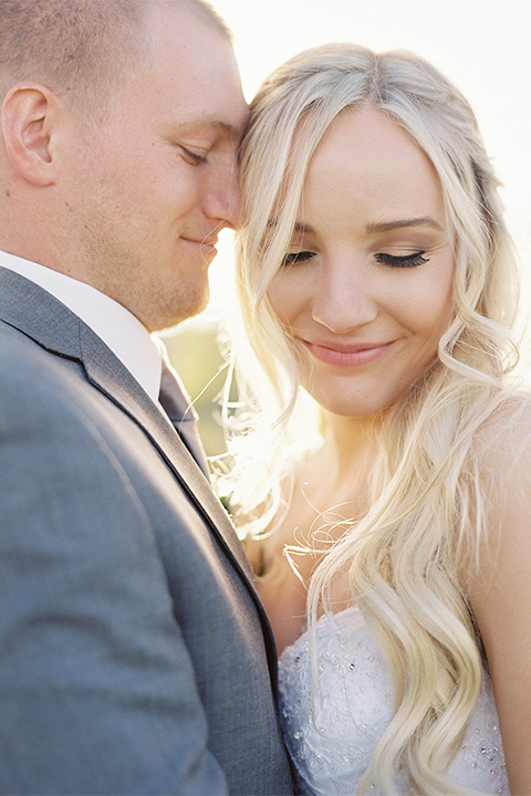 Southern california wedding at riverview free church bride strapless ball gown with a sweetheart neckline and tulle skirt with a long veil and braided hairstyle with groom grey notch lapel suit with matching vest and white dress shirt with long grey tie and light blue and green floral boutonniere hugging close up