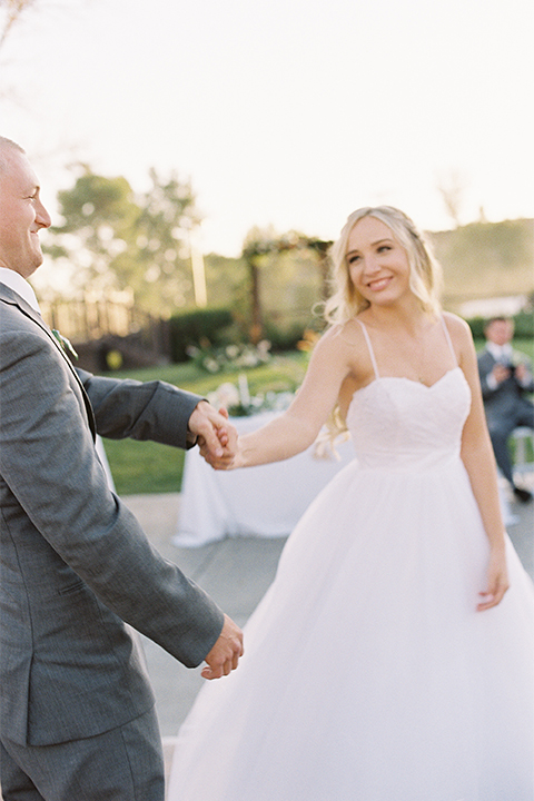 Southern california wedding at riverview free church bride strapless ball gown with a sweetheart neckline and tulle skirt with a long veil and braided hairstyle with groom grey notch lapel suit with matching vest and white dress shirt with long grey tie and light blue and green floral boutonniere holding hands and dancing