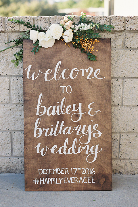 Southern california outdoor wedding at the riverview free church wedding welcome sign light brown wood sign with white calligraphy writing rustic decor with white and green flowers on top wedding photo idea for decor