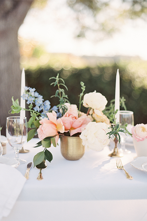 Southern california outdoor wedding at the riverview free church wedding welcome sign light brown wood sign with white calligraphy writing rustic decor with white and green flowers on top with table white linen and white place settings with tall white candles and gold holders with light orange and white flower centerpiece decor with gold vases and gold silverware