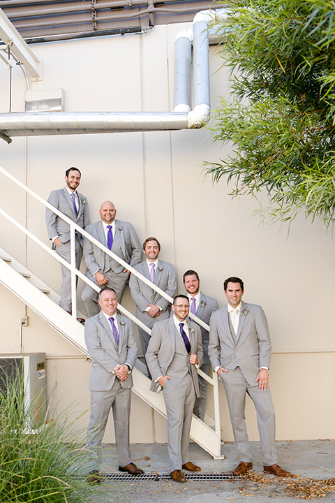 Temecula outdoor wedding at callaway winery groom heather grey notch lapel suit with matching vest and white dress shirt with a long white tie and light purple floral boutonniere standing with groomsmen heather grey suits with long purple ties