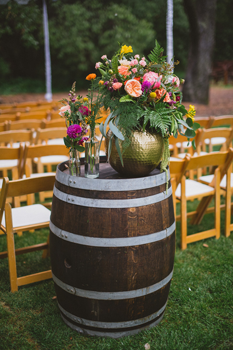 Temecula outdoor wedding at temecula creek inn ceremony set up with brown and white chairs with wine barrels and colorful flowers on top with clear tent covering the rain on grass wedding photo idea for ceremony set up