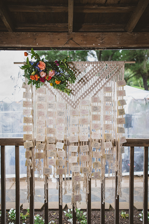Temecula outdoor wedding at temecula creek inn table set up light brown wood table with matching wood chairs and colorful flower centerpiece decor with colorful glassware and white place settings with brown wood table numbers with white calligraphy writing