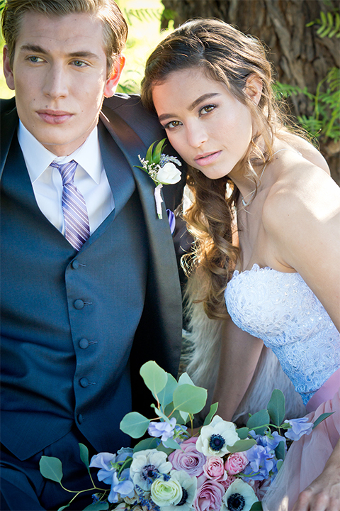 San diego outdoor woodland wedding shoot bride blush pink chiffon strapless gown with a sweetheart neckline and groom navy blue shawl lapel tuxedo with a matching vest and white dress shirt with a long pink striped tie and white floral boutonniere sitting and hugging close up